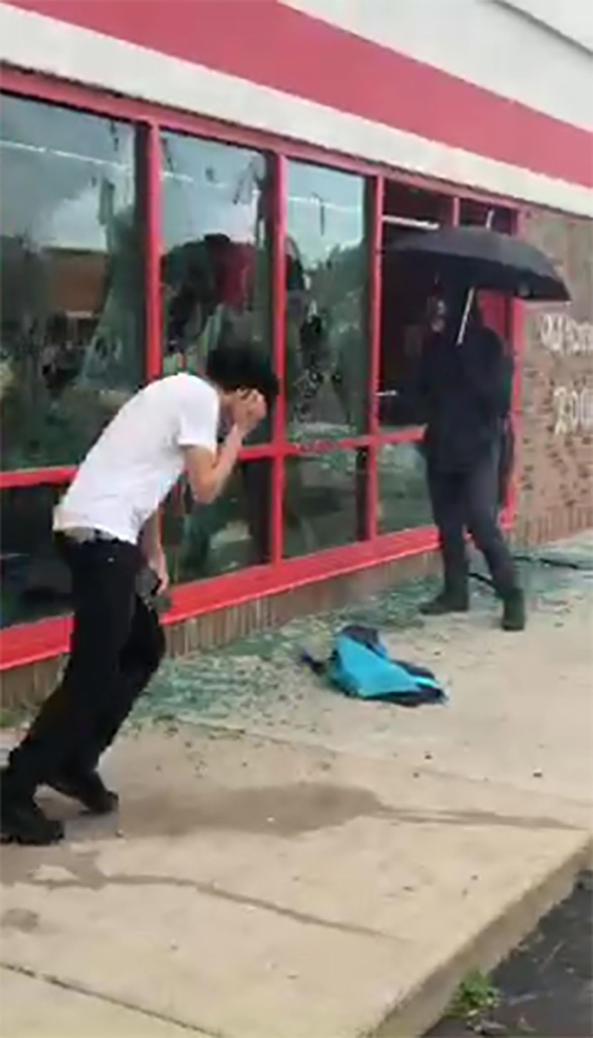 PHOTO: A man carrying an umbrella smashes windows at a store in Minneapolis, during protests following the death of George Floyd in May 2020.