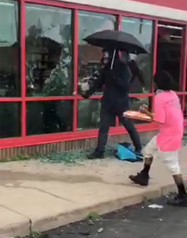 PHOTO: A man carrying an umbrella smashes windows at a store in Minneapolis, during protests following the death of George Floyd in May 2020.