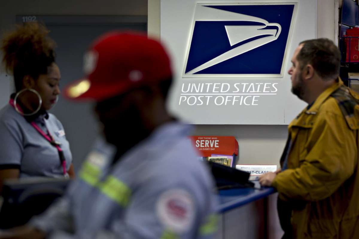 PHOTO: Signage is seen past customers and a postal clerk, left, at the United States Postal Service (USPS) Joseph Curseen Jr. and Thomas Morris Jr. post office station in Washington, D.C., Dec. 12, 2017. 