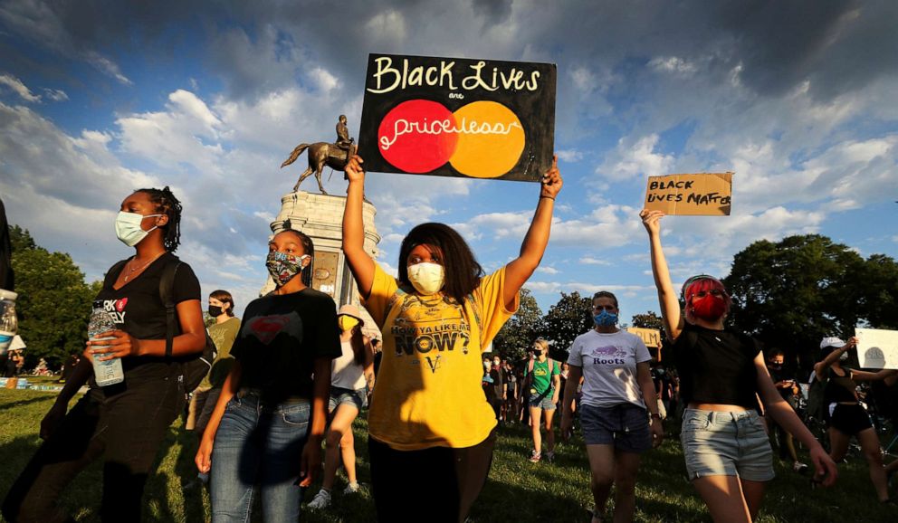 PHOTO: Protesters hold signs while walking away from the Lee statue on Monument Avenue, in Richmond, Va., June 3, 2020.