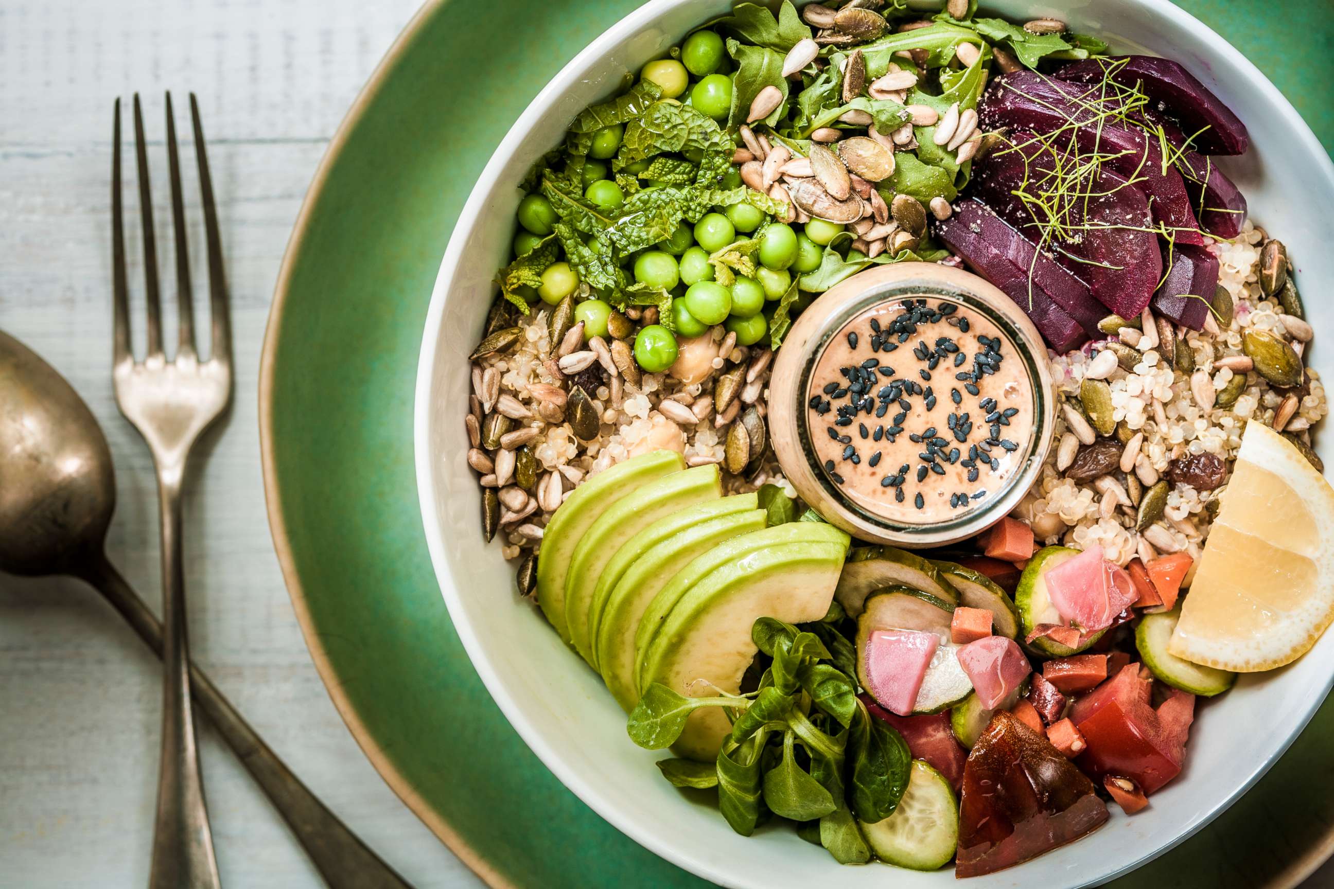 PHOTO: A vegan lunch bowl containing leafy greens, grains, seeds, vegetables, avocado and a peanut-miso sauce.