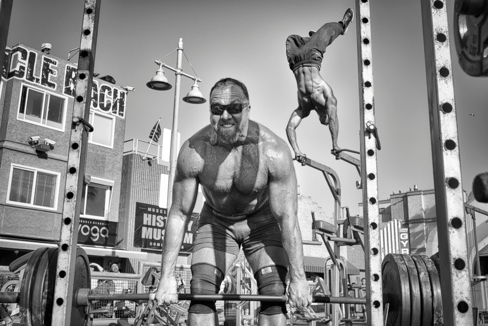 PHOTO: Muscle Beach Gym - A weightlifter lifts a barbell loaded with heavy plates while a bodybuilder performs an aerial handstand at the Muscle Beach Gym in Venice Beach, Calif., April 1, 2016.