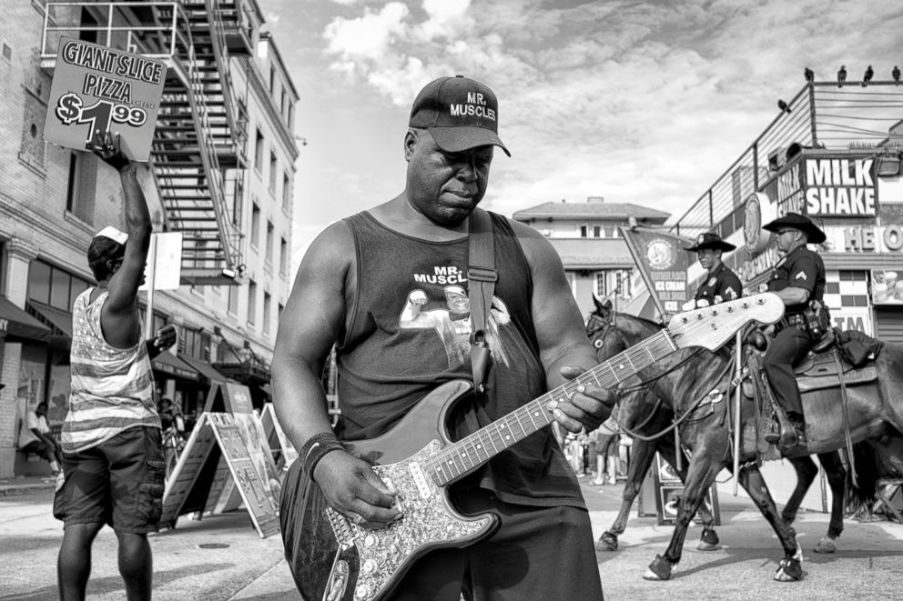 PHOTO: Mr. Muscles - "If it wasn't for the price of pizza revealing the contemporary nature of the  scene, one could mistake this photograph for a slice of 1970's Americana, complete with Blues music and policemen on horses," comments, photographer Saguy.