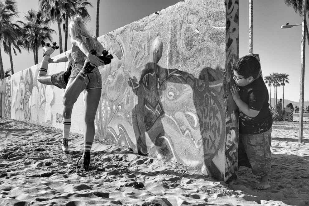 PHOTO: Graffiti Wall - A little boy who came with his family to paint on the Venice Art Walls  mischievously peeks at two teenage girls on roller skates posing for pictures.