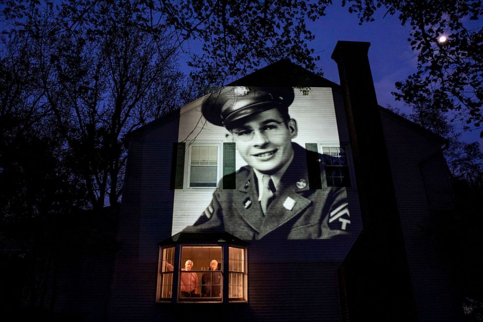 PHOTO: An image of veteran James Sullivan is projected onto the home of his son, Tom Sullivan, left, as he looks out a window with his brother, Joseph Sullivan, in South Hadley, Mass., May 4, 2020. 