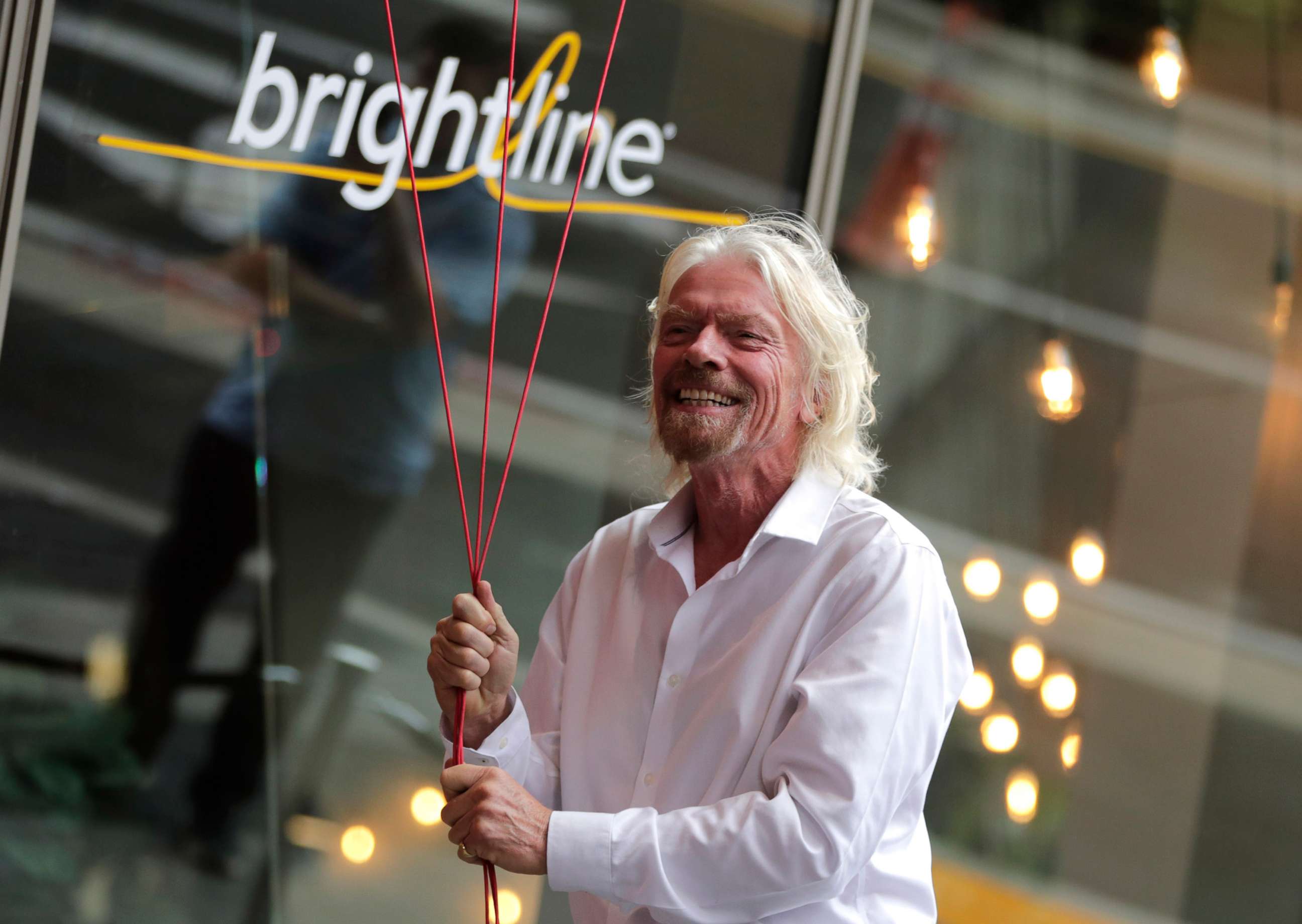 PHOTO: In this April 4, 2019, file photo, Richard Branson, of Virgin Group, prepares to unfurl a banner during a naming ceremony for the Brightline train station, to be renamed as Virgin MiamiCentral, in Miami.