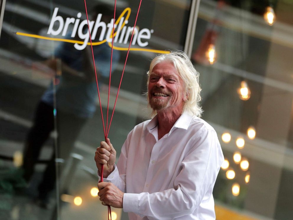 PHOTO: In this April 4, 2019, file photo, Richard Branson, of Virgin Group, prepares to unfurl a banner during a naming ceremony for the Brightline train station, to be renamed as Virgin MiamiCentral, in Miami.