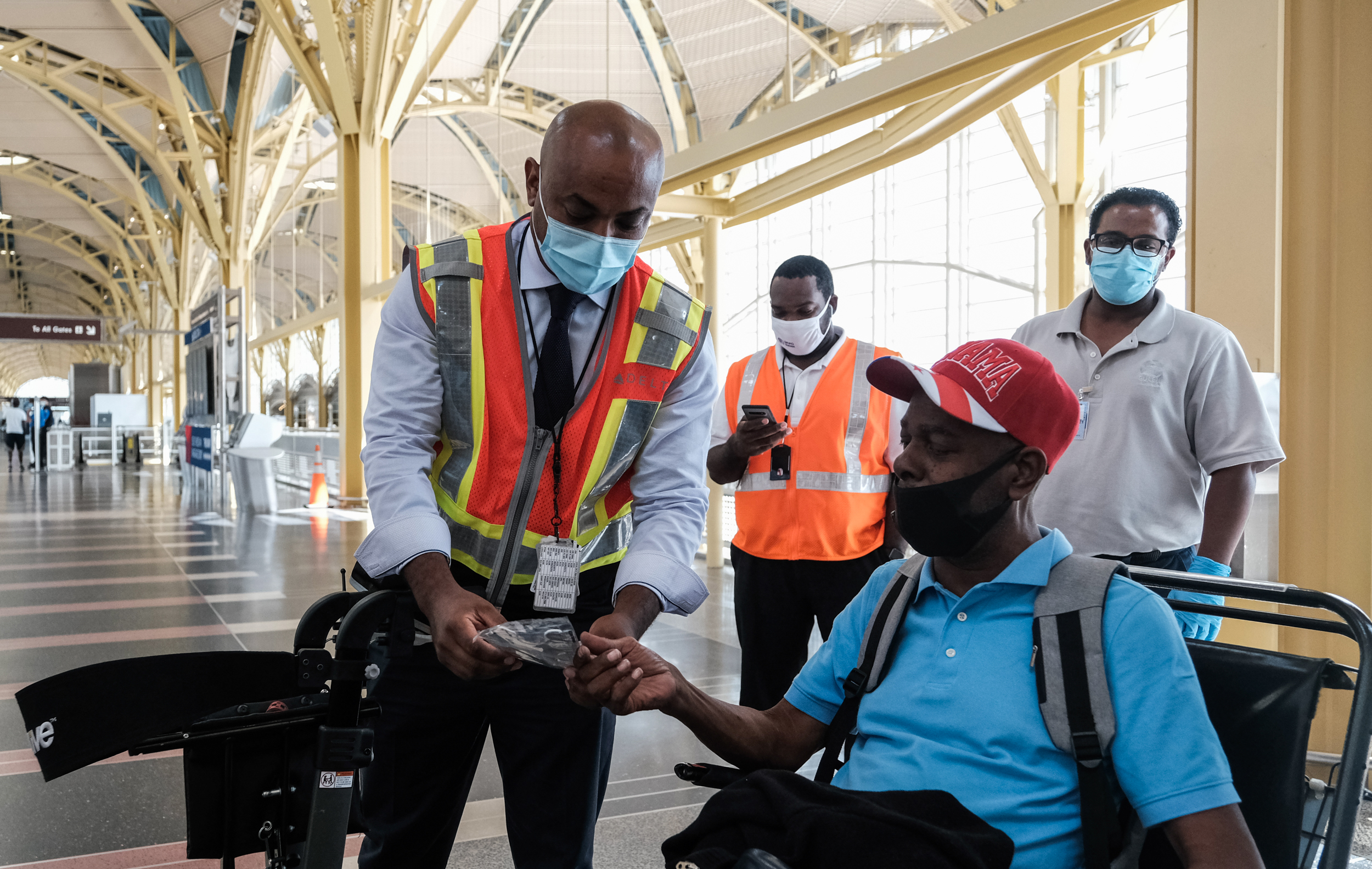 PHOTO: A Delta Airline employee gives a face mask to a passenger during check in at the Ronald Reagan National Airport on July 22, 2020, in Arlington, Va.