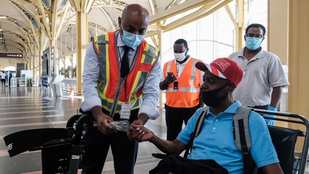 PHOTO: A Delta Airline employee gives a face mask to a passenger during check in at the Ronald Reagan National Airport on July 22, 2020, in Arlington, Va.