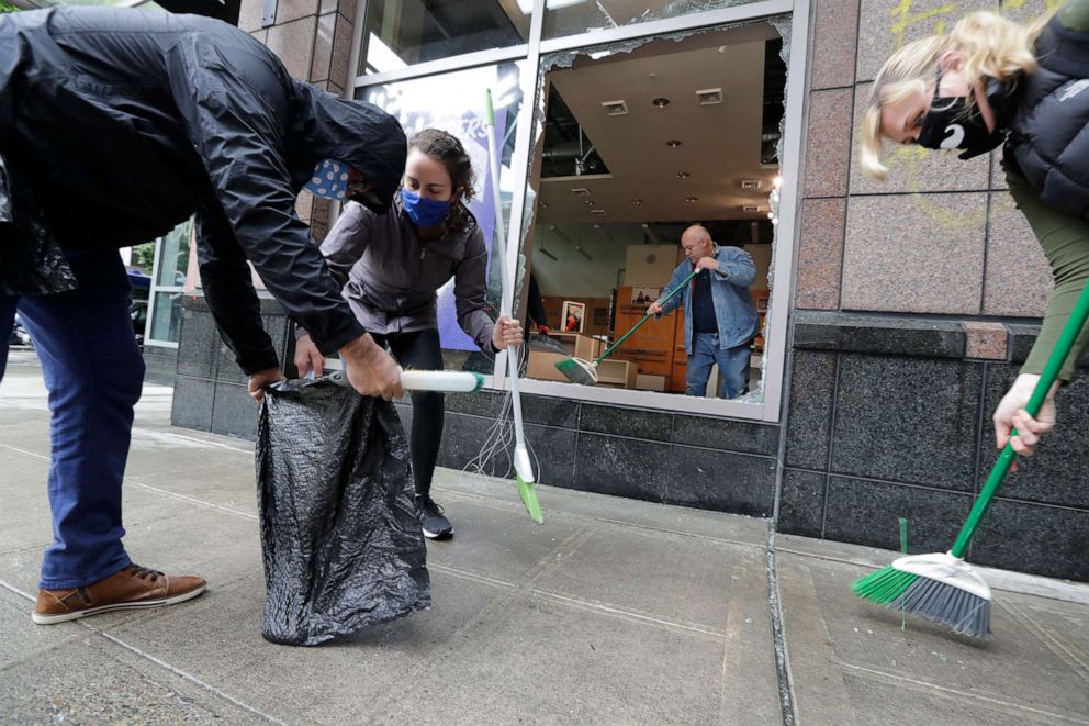 PHOTO: Volunteers sweep broken glass outside as a man cleans up inside a smashed-out store, May 31, 2020, in Seattle, following protests the night before over the death of George Floyd, a black man who was in police custody in Minneapolis.