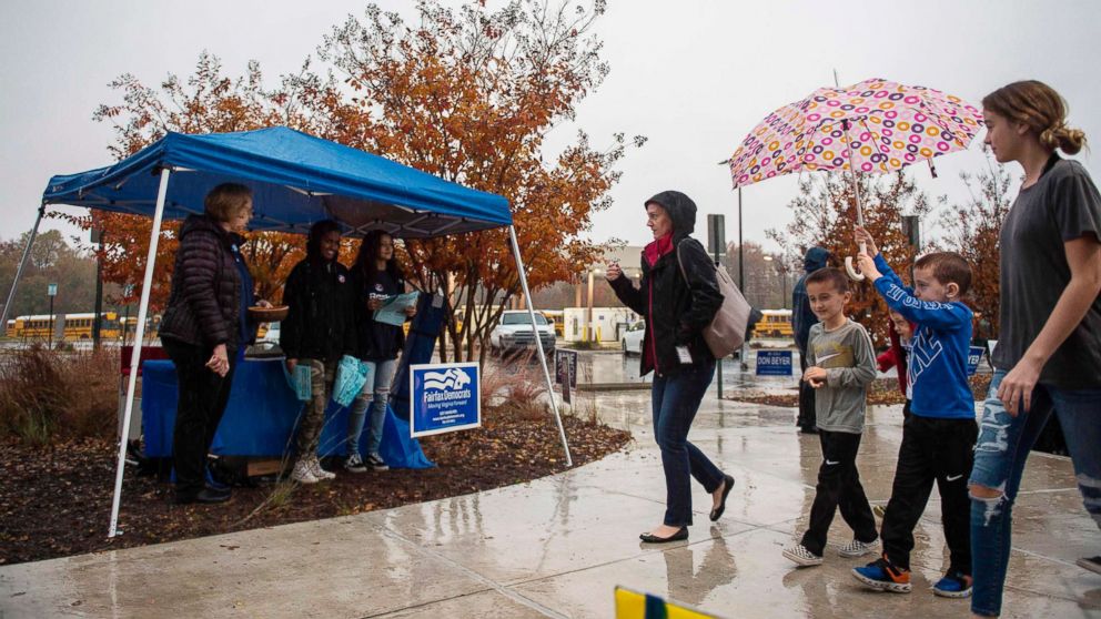 PHOTO: A family walks past volunteers with the Democratic party as they walk to a polling station during the mid-term elections at the Fairfax County bus garage in Lorton, Va., Nov. 6, 2018.
