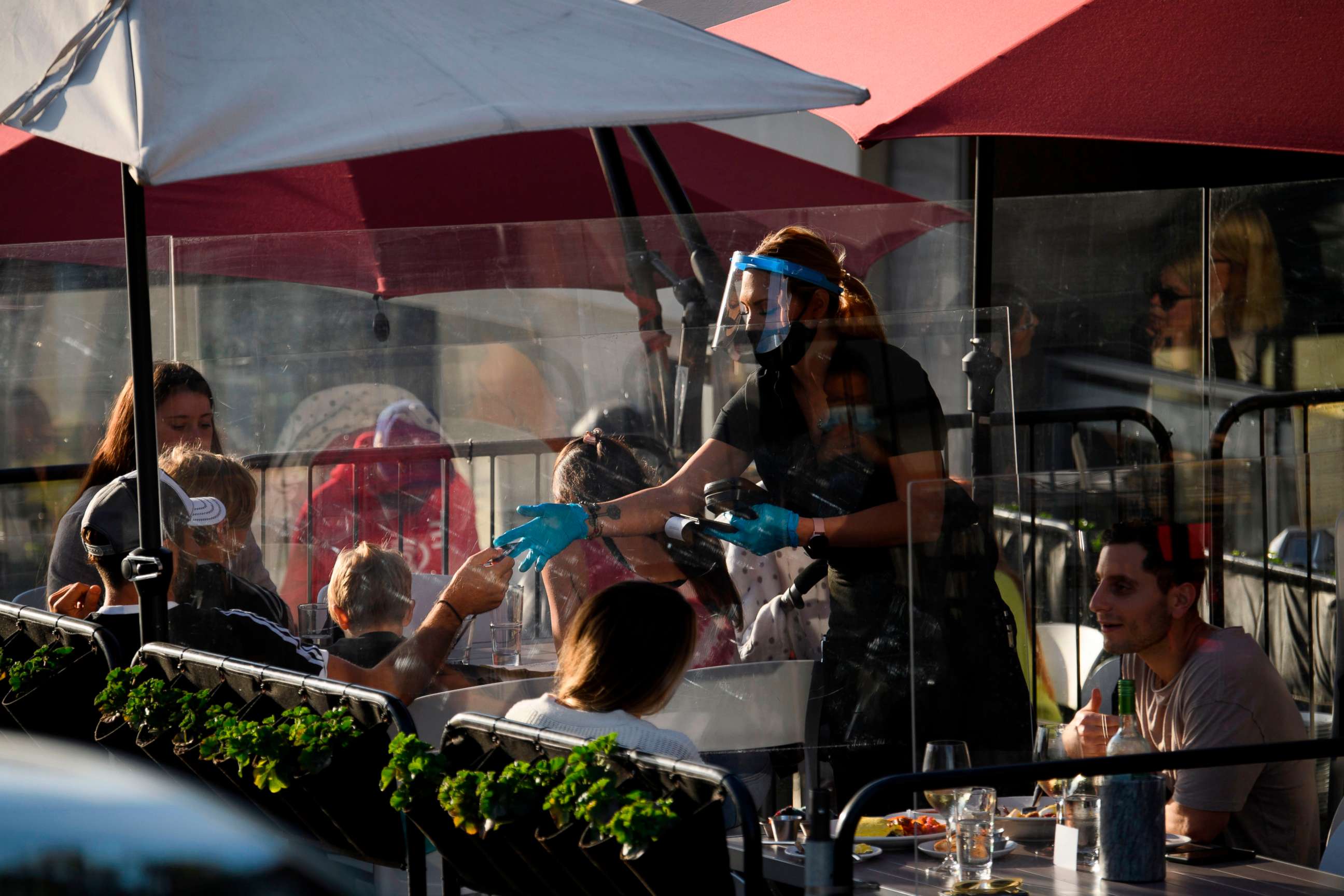 PHOTO: A waiter wearing personal protective equipment (PPE) returns a credit card to a customer dining outdoors in Manhattan Beach, California, on Nov. 21, 2020.