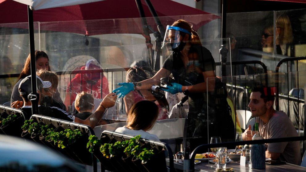 PHOTO: A waiter wearing personal protective equipment (PPE) returns a credit card to a customer dining outdoors in Manhattan Beach, California, on Nov. 21, 2020.