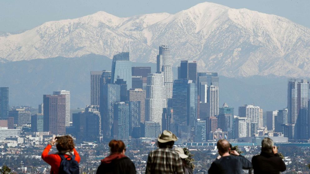 PHOTO: People look at the snow-covered San Gabriel Mountains as they appear behind the skyline of Los Angeles, Mar. 2, 2023.