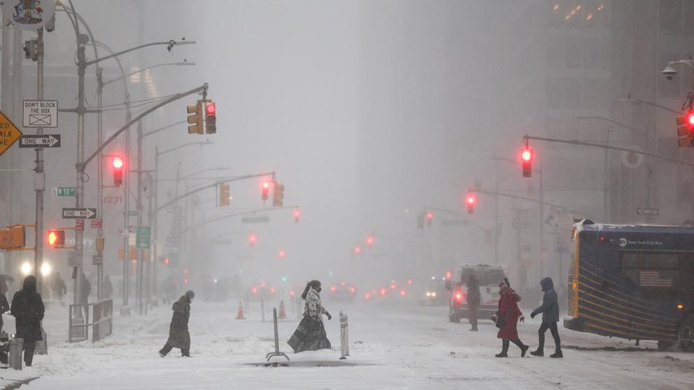 PHOTO: People walk across Sixth Avenue as snow falls in the Manhattan borough of New York City on January 25, 2026.