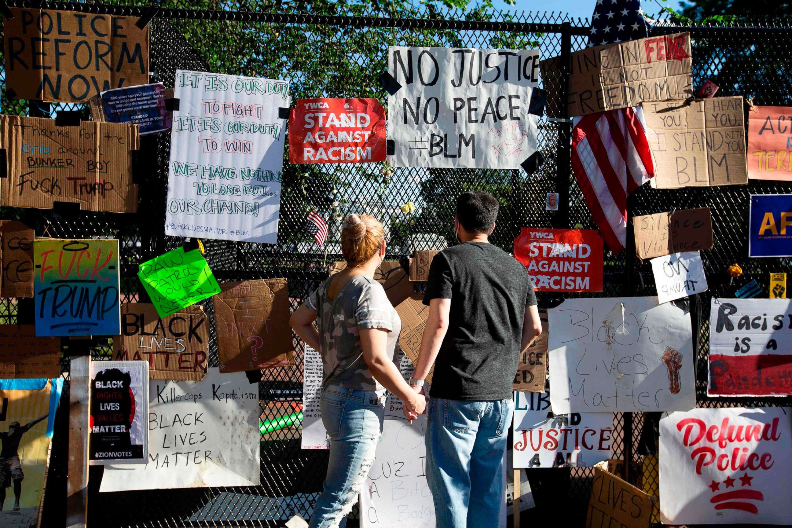 PHOTO: A couple reads signs hung on a fence at Lafayette Square near the White House, during ongoing protests against police brutality and racism, June 7, 2020, in Washington, D.C.