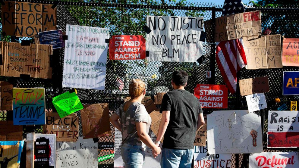 PHOTO: A couple reads signs hung on a fence at Lafayette Square near the White House, during ongoing protests against police brutality and racism, June 7, 2020, in Washington, D.C.
