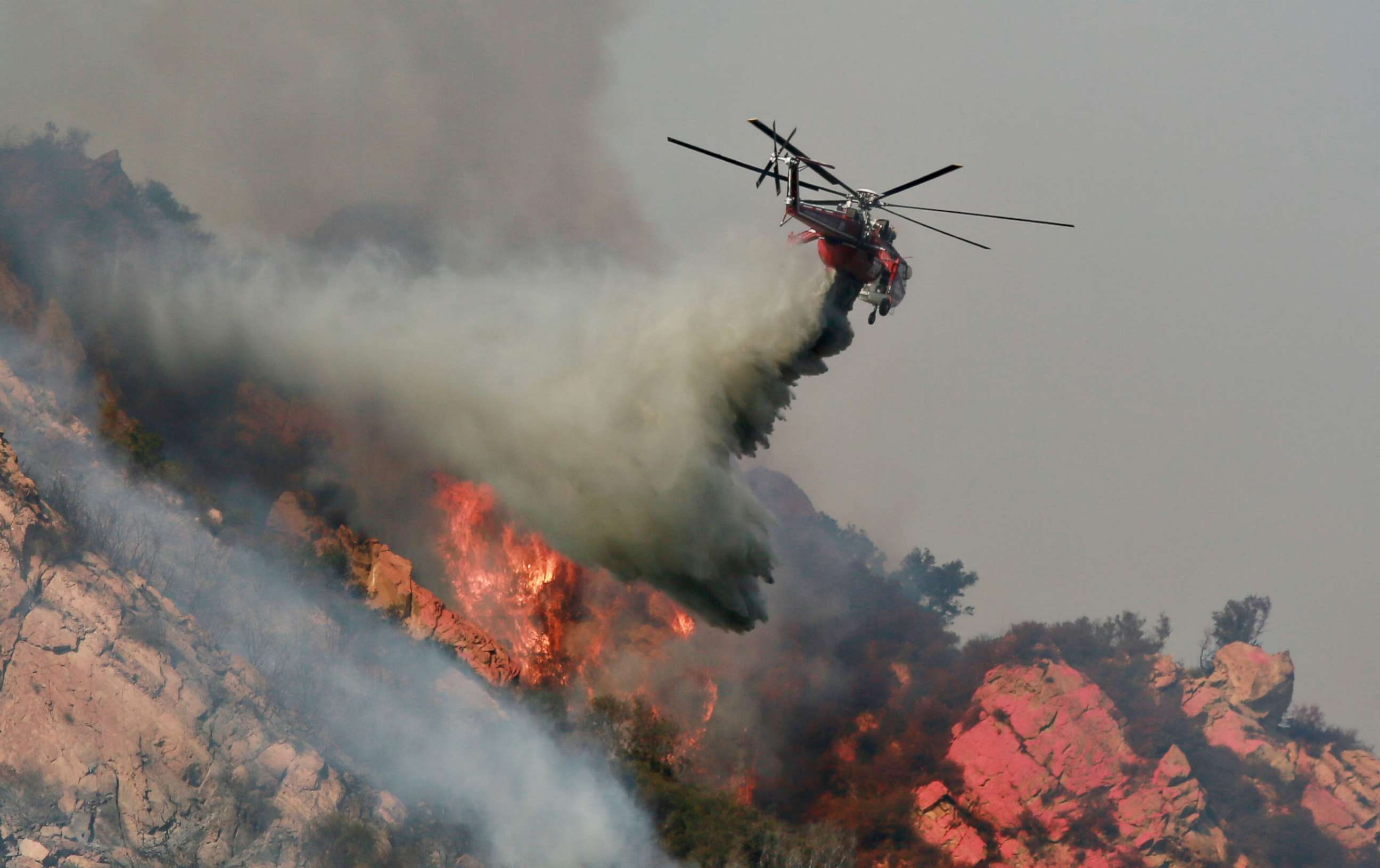 PHOTO: A helicopter drops flame retardant on a wildfire, Nov. 10, 2018, in Malibu, Calif. The Woolsey fire has burned over 70,000 acres and has reached the Pacific Coast as it continues grow.