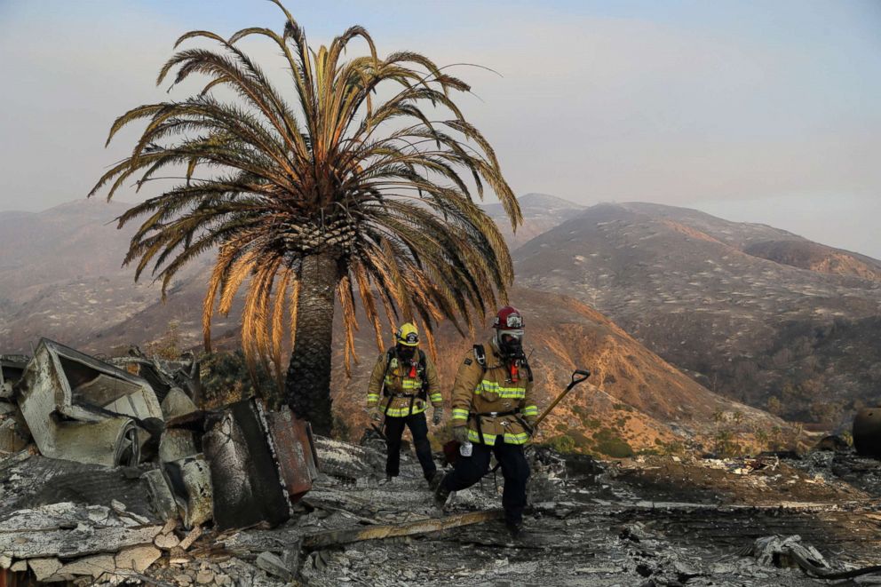PHOTO: Firefighters Jason Toole, right, and Brent McGill with the Santa Barbara Fire Dept. walk among the ashes of a wildfire-ravaged home after turning off an open gas line, Nov. 10, 2018, in Malibu, Calif.