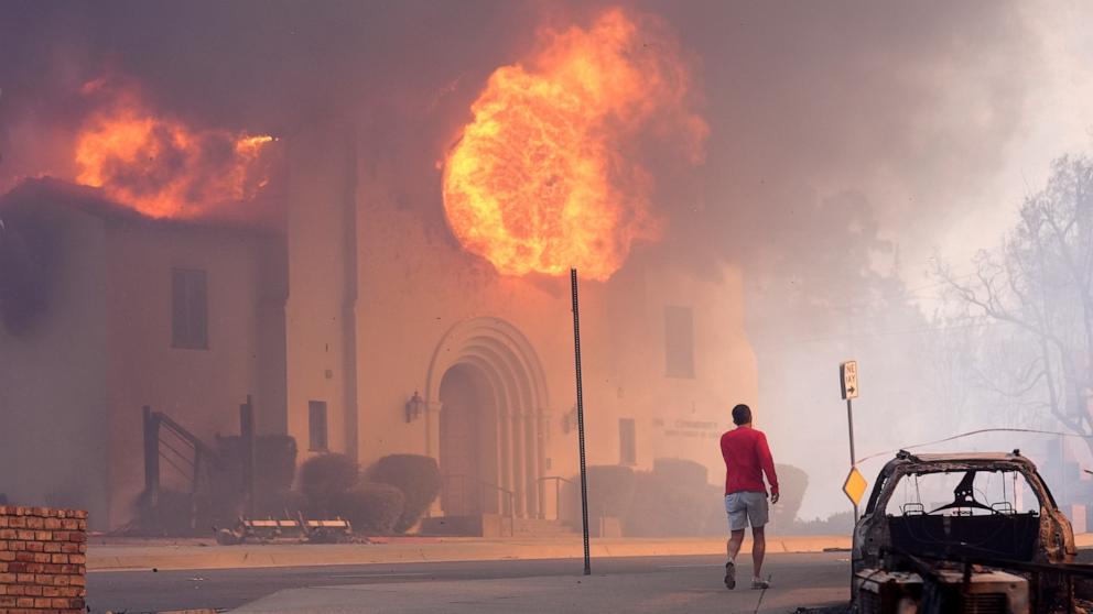 PHOTO: A pedestrian walks across from the burning Altadena Community Church, Jan. 8, 2025, in the downtown Altadena section of Pasadena, Calif.