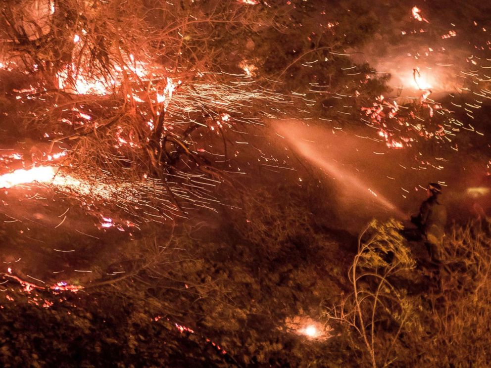PHOTO: A man uses a hose to extinguish the Creek Fire as it burns along a hillside near homes and horses in the Shadow Hills neighborhood of Los Angeles, Calif., on Dec. 5, 2017.