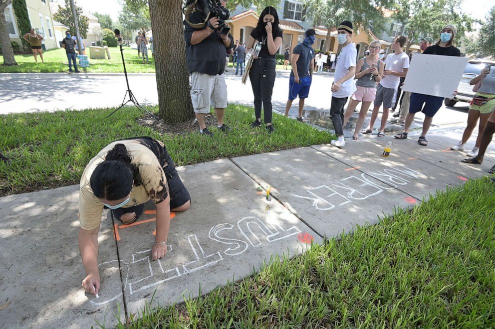 PHOTO: Protester Taylor Dimuzio writes a message with chalk on a sidewalk in front of a townhouse owned by Minneapolis police officer Derek Chauvin, May 29, 2020, in Windermere, Fla.