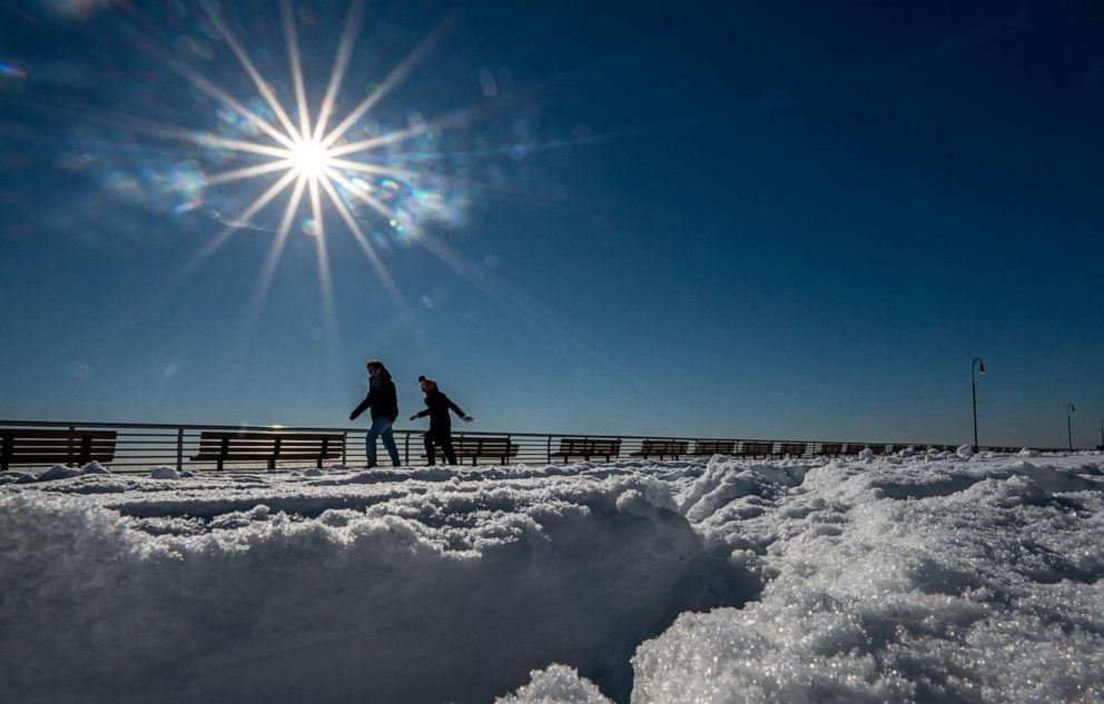 PHOTO: Two people walk on the boardwalk with snow on the ground on in Long Beach, N.Y., Jan. 8, 2022.