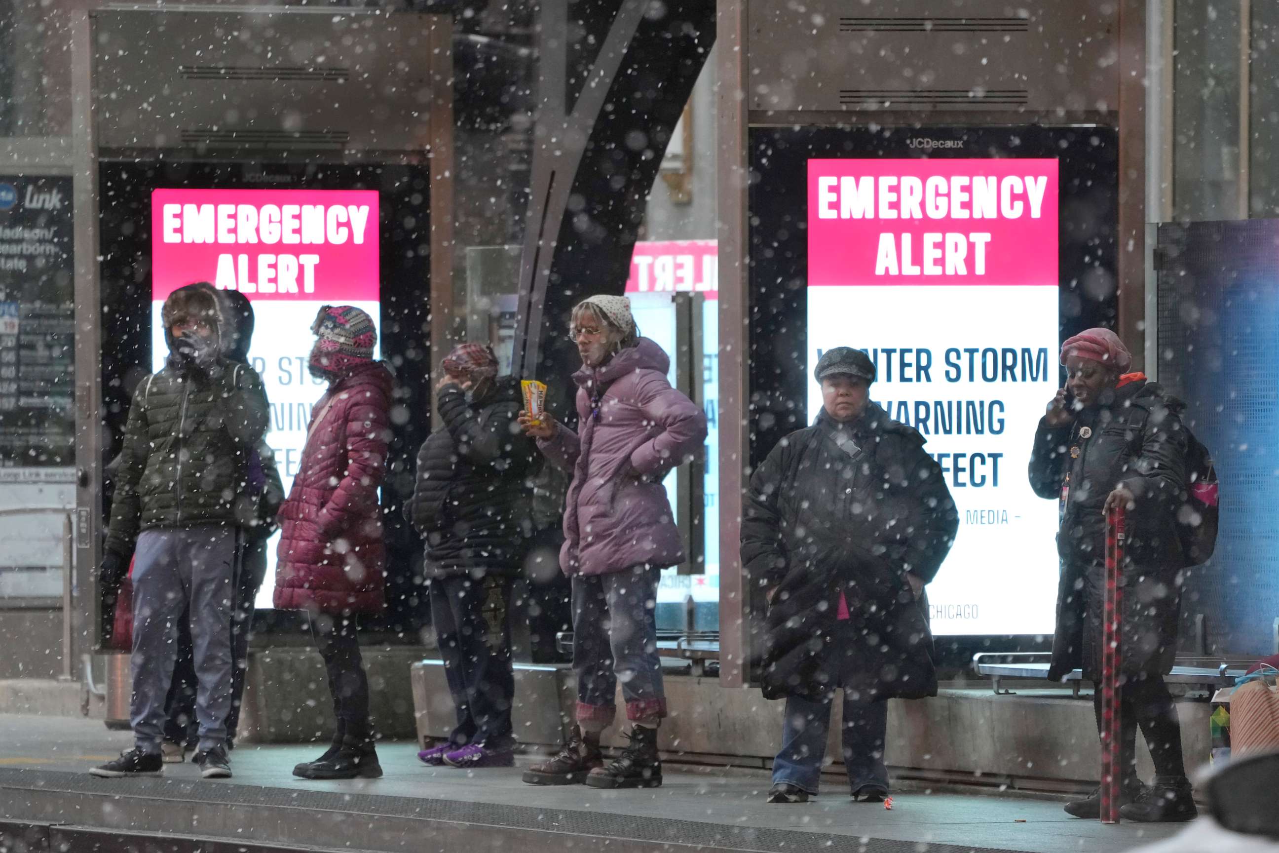 PHOTO: Bus riders wait at a sheltered stop in Chicago's Loop as snow falls and a public service message reminds riders of the winter storm in Chicago, Dec. 22, 2022.