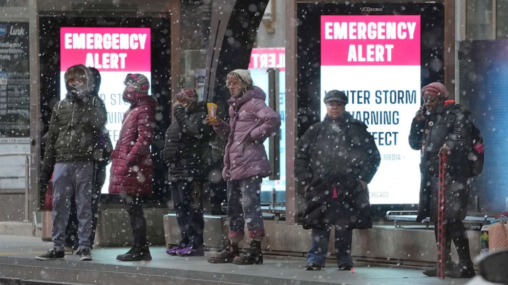 PHOTO: Bus riders wait at a sheltered stop in Chicago's Loop as snow falls and a public service message reminds riders of the winter storm in Chicago, Dec. 22, 2022.