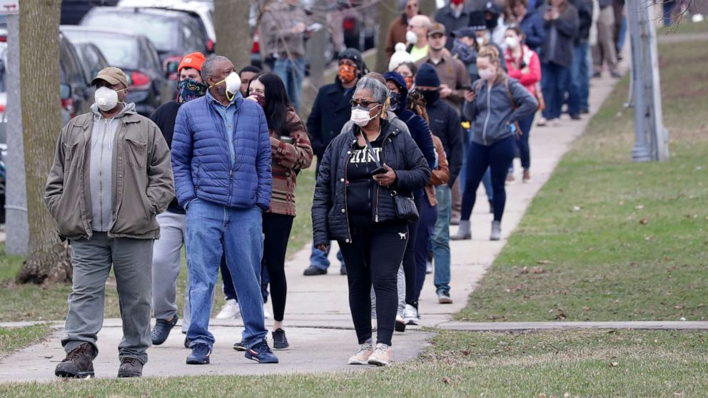 PHOTO: In this April 7, 2020, file photo, people wait in a line to vote in the presidential primary election while wearing masks and practicing social distancing at Riverside High School in Milwaukee.