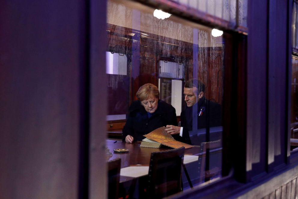 PHOTO: German Chancellor Angela Merkel and French President Emmanuel Macron look at a guest book inside a replica of the wagon where the Armistice was signed in 1918, in the Clairiere of Rethondes, in Compiegne, France, Nov. 10, 2018.