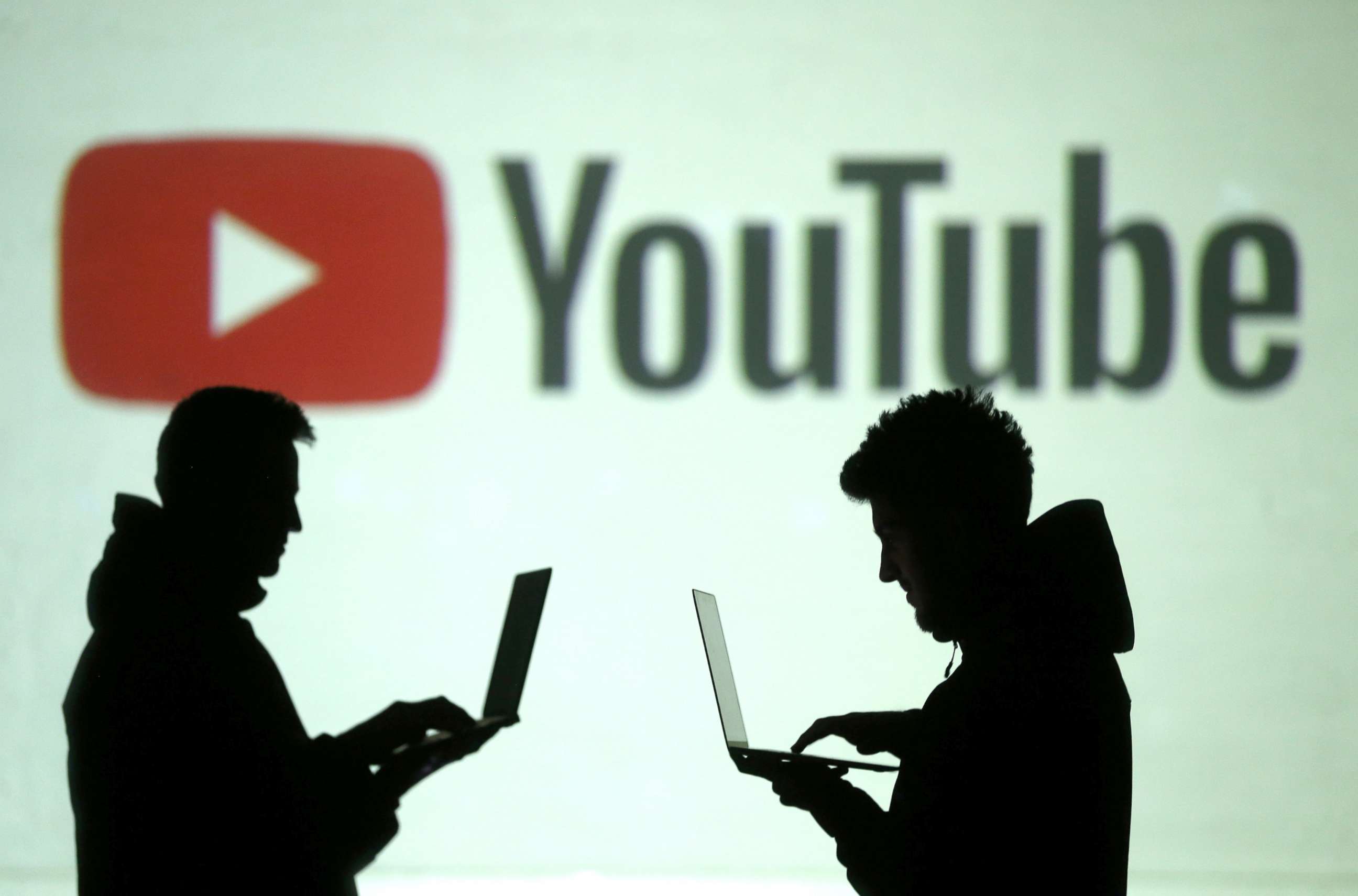 PHOTO: Silhouettes of mobile device users are seen next to a screen projection of Youtube logo, March 28, 2018.