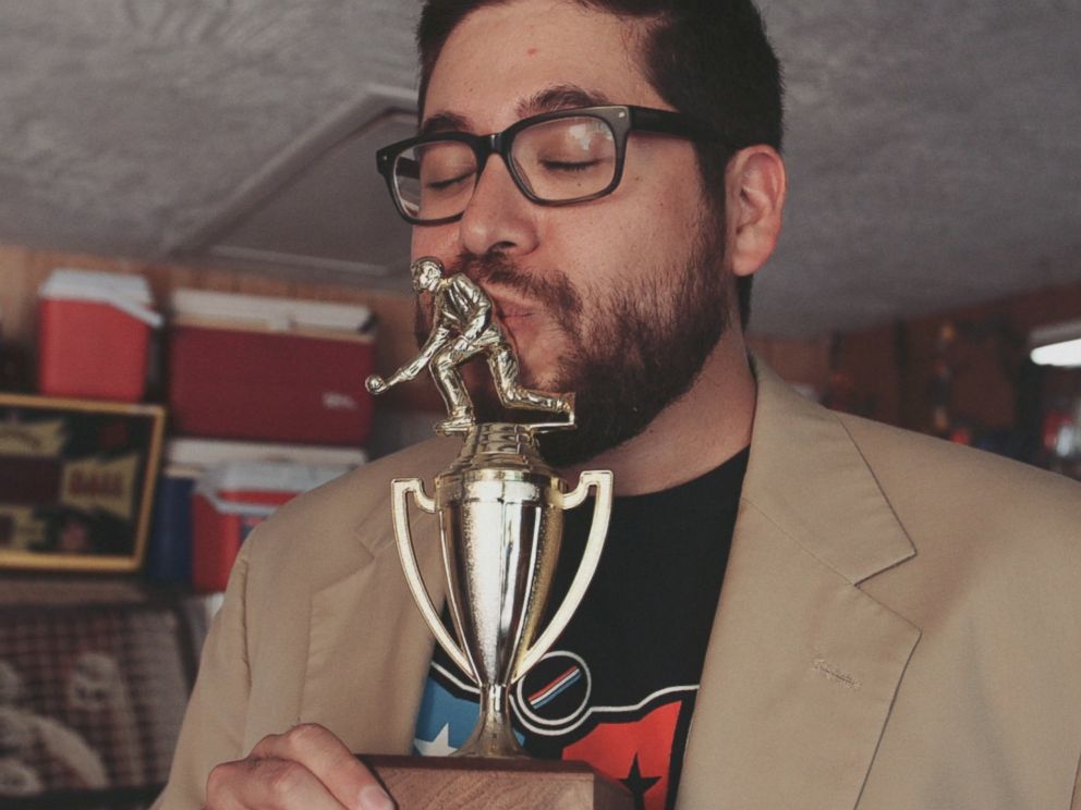 PHOTO: Skee-Ball champion Roy Brewbacca Hinojosa wearing his cream-colored jacket and kissing his trophy in Austin, Texas.