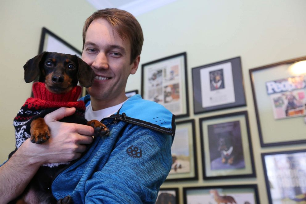 PHOTO: Ryan Beauchesne holds his dog, Crusoe, in front of the pup's wall of fame, featuring a collection of work he's done.