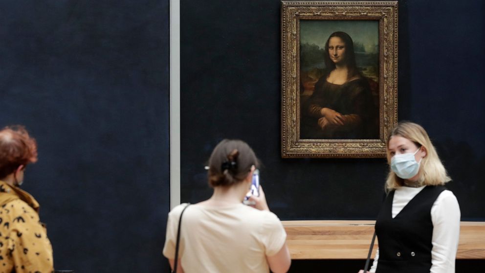 FILE - Visitors pose in front of Leonardo da Vinci's Mona Lisa in the Louvre museum, Wednesday, May, 19, 2021 in Paris. A man seemingly disguised as an old woman in a wheelchair threw a piece of cake at the glass protecting the Mona Lisa on Sunday Ma